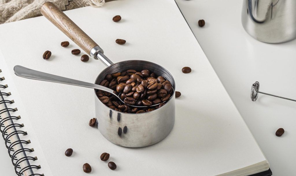 alto angulo do notebook com uma xicara de graos de cafe torrados 1